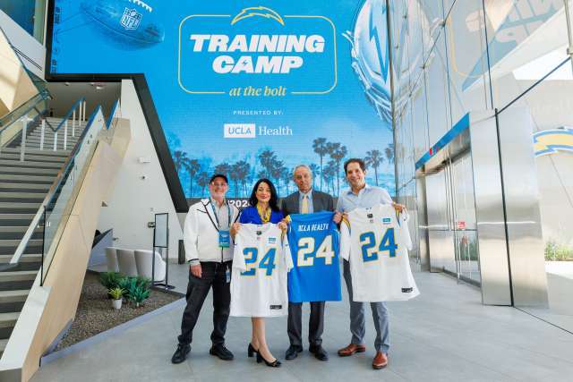 Fred Maas, Johnese Spisso, Dr. John Mazziotta, and Dr. Nicholas Bernthal at Los Angeles Chargers training camp, holding chargers t-shirts with the number 24.