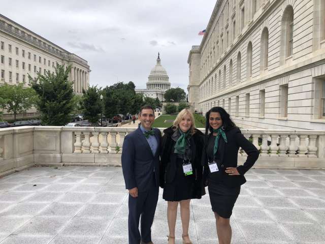 Three people smiling and facing the camera with the nation's capitol building in the background