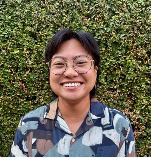 headshot of Katherine Santos wearing glasses and a patterned shirt with a hedge as the background