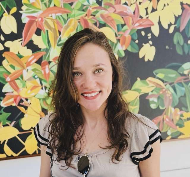 Smiling woman with wavy brown hair in front of bright floral mural