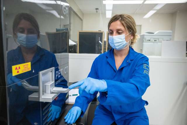 A technician in a blue lab coat operates equipment in a laboratory setting.