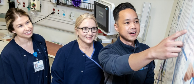 Three students in an exam room looking at a chart.