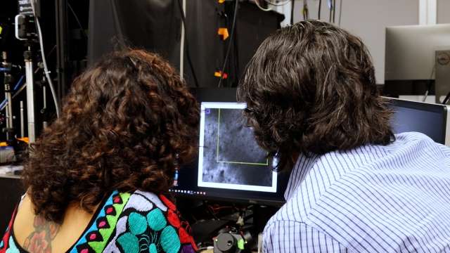 Two people leaning over a monitor displaying a grayscale image.
