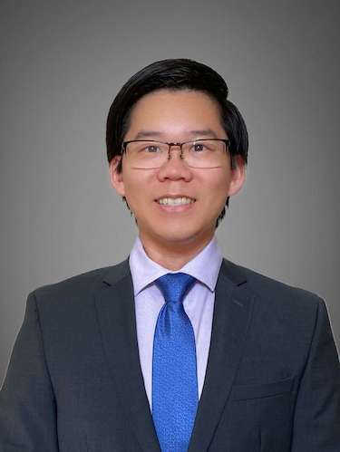  A headshot of Aaron Wang, a smiling man with short dark hair and glasses, wearing a dark suit and a bright blue tie.
