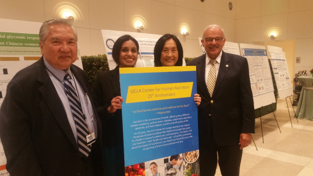 Four people, two men and two women, posing with a poster of the UCLA center of human nutrition 25th anniversary