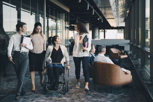 A group of people talking. One person is in a wheelchair and three are walking.