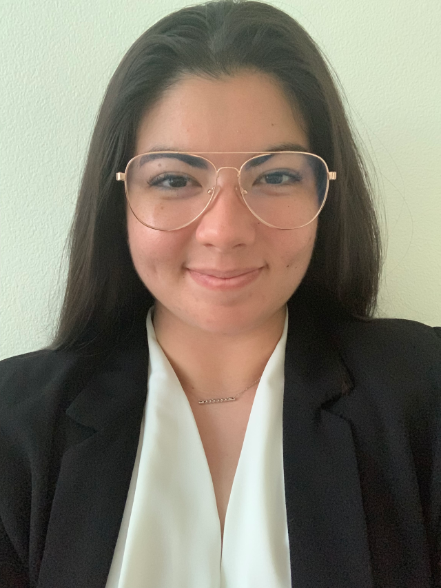 Smiling professional wearing clear glasses and a black blazer against a light wall