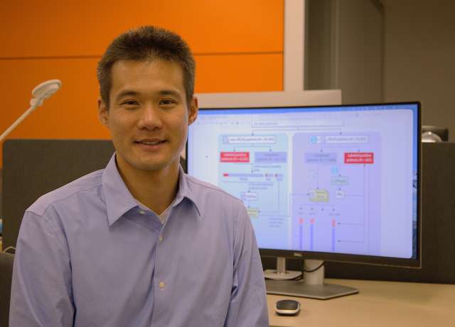 Person seated smiling before a monitor displaying a flowchart diagram