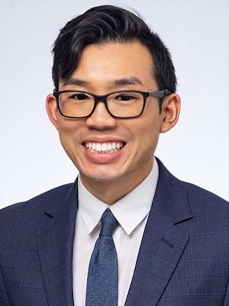 Dr. Justin Tram wearing glasses and a blue suit