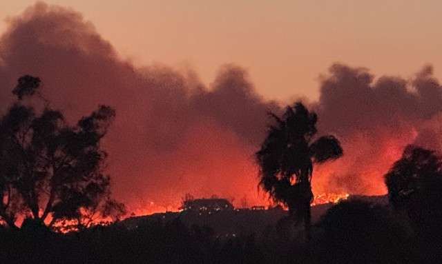 wildfire burning over mountain with trees, smoke, and fire in the background