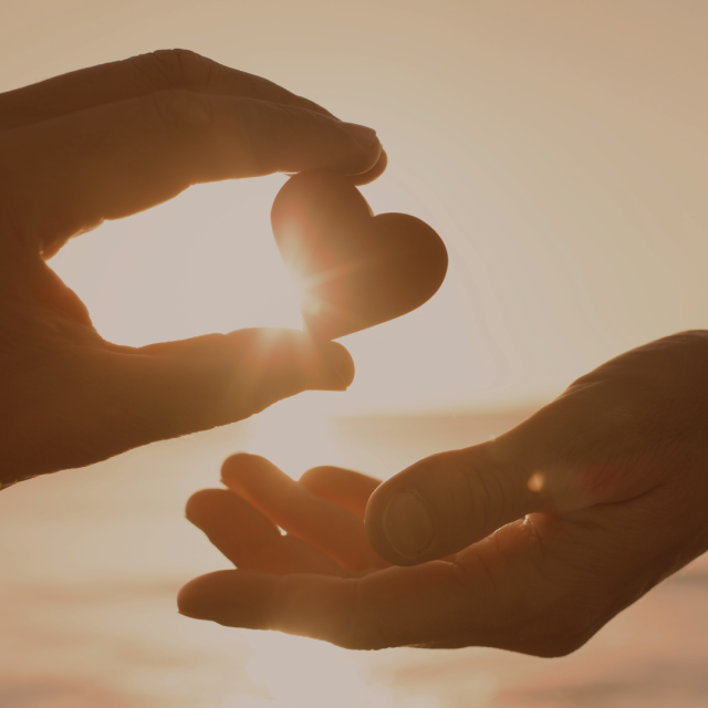 Hands passing a small heart shape in warm sunlight