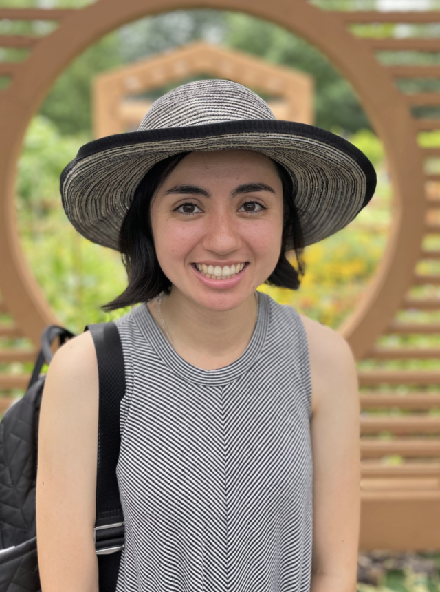 Young woman wearing a wide-brimmed hat and a striped tank top, standing outdoors.