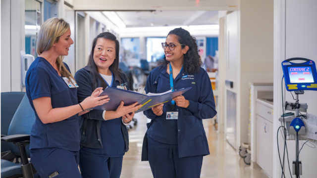 A group of nurses gathered on the unit hallway having a conversation about a topic related to a banner they are holding in their hands.