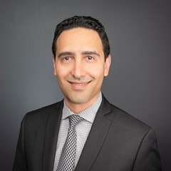 A smiling man with dark hair and a dark suit.