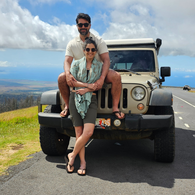 Jose Hernandez Carcamo and wife, Pamela, in Maui standing in front of jeep. The jeep is pulled over the side of the road, overlooking a scenic view.