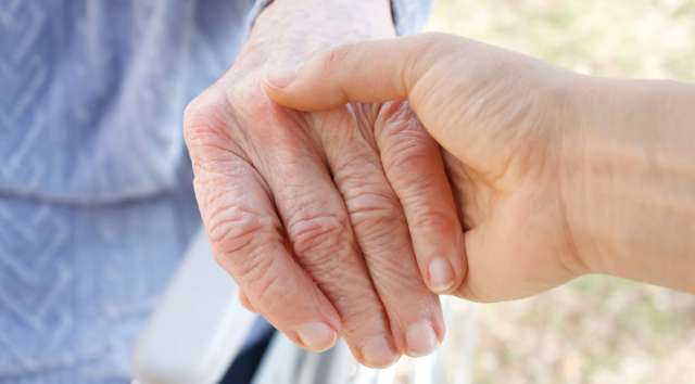 A young person holding an older person in a wheelchair by the hand