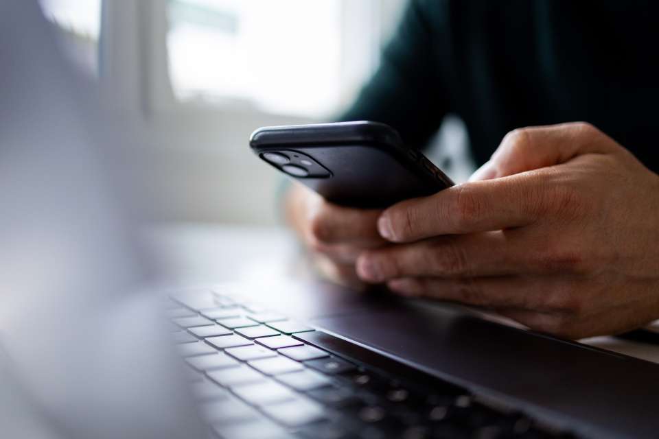 Man holding a smartphone and sitting in front of his computer