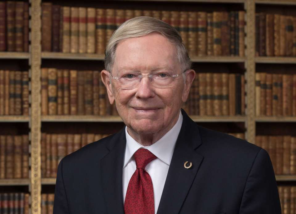Portrait of Dr. Bradley R. Straatsma, JD wering a dark suit with a red tie standing in front of library shelves in an executive conference room.jpg