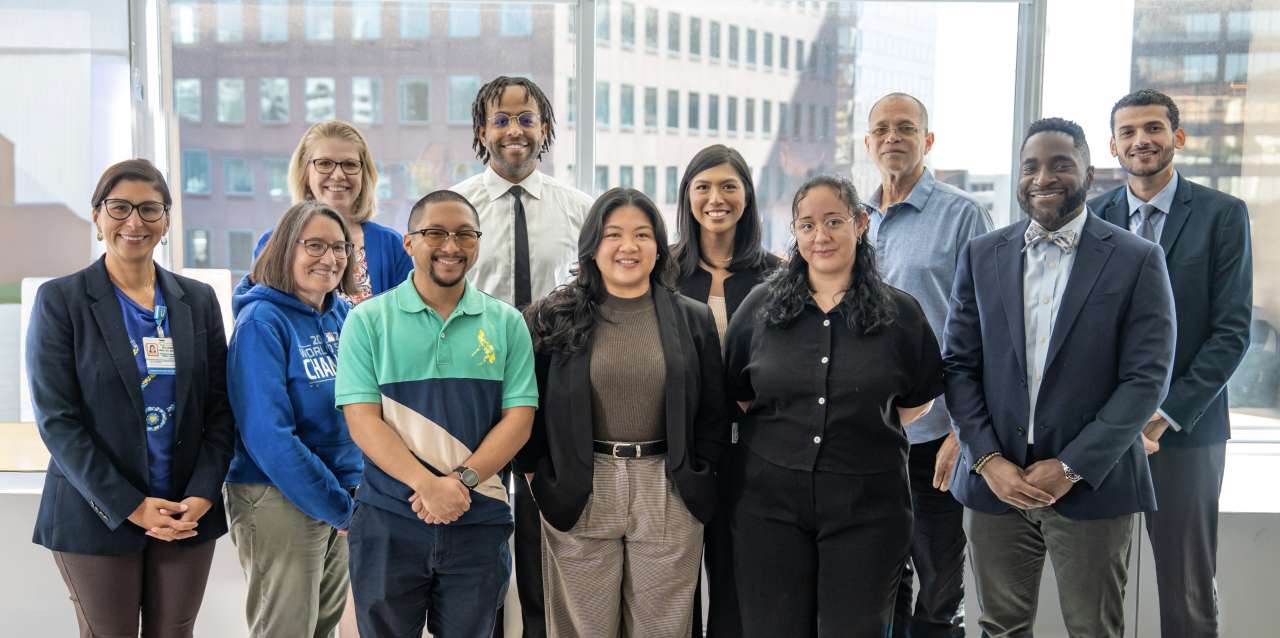 Community engagement and inclusice excellence team of 11 people smiling with buildings in the background.
