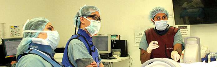Three medical professionals in scrubs and masks discussing in a clinical setting.