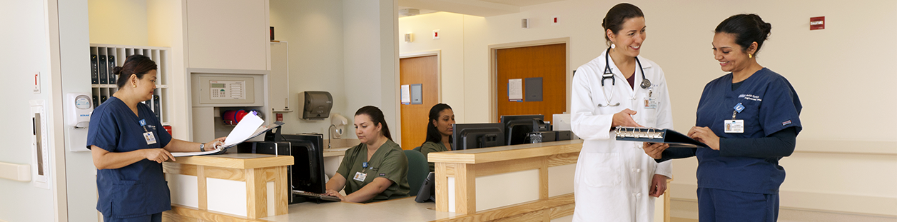 The image depicts a group of UCLA Health nurses working together in a hospital setting. They are dressed in matching navy blue scrubs.