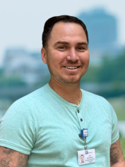 Male UCLA Health employee smiling outdoors, wearing light green shirt and an ID badge.