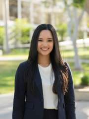 A headshot of Rejah Marie Nabong, a woman with long dark hair, smiling and wearing a dark blazer over a white top