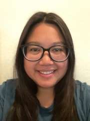 Emy Arango with long brown hair, smiling wearing glasses