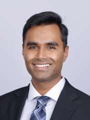  A headshot of Vishnu Murthy, a man with short dark hair, smiling and wearing a black suit jacket, white shirt, and patterned blue tie.