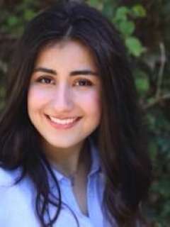 Noor Jahanshahi smiling with long dark hair, wearing a light blue shirt. Her genuine smile conveys confidence and approachability.