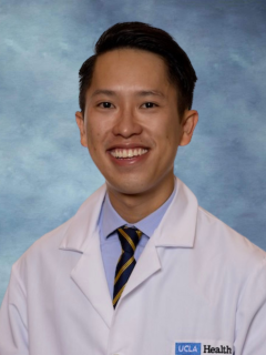 A headshot of Dr. Thang Tran who has short dark brown hair, wearing a white lab coat, tie and smiling
