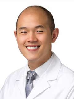 Dr. Michael Oh wearing a lab coat and smiling in front of a white background