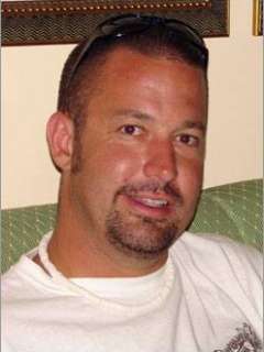 Jim sitting on a green couch wearing a white t-shirt