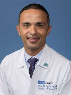 Headshot of a Dr. David Sayah in white coat and tie against a blue background