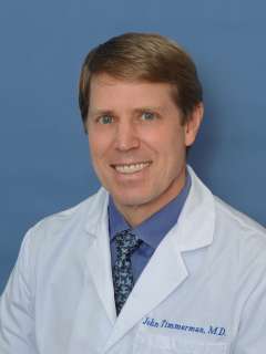 John M. Timmerman, MD wearing a white coat and tie, smiling
