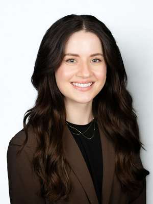 Smiling woman in professional headshot wearing brown blazer and layered necklaces