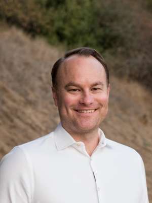 Robert Yeilding in a white shirt smiling and looking at camera in front of a dirt hill