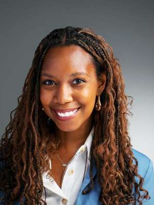 Smiling professional headshot of person with long locs wearing blue blazer