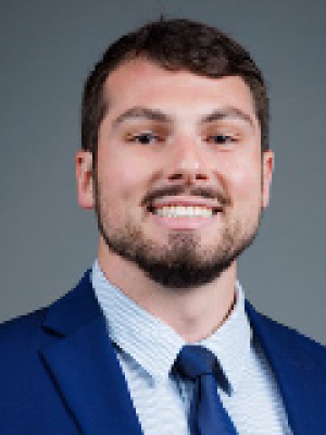 Smiling man with short beard in blue suit and tie on gray background