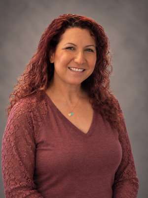 Talin Mirzaians smiling with curly red hair wearing maroon V-neck sweater and pendant
