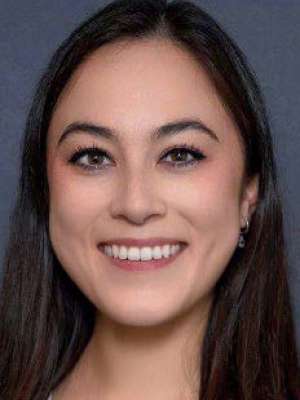 Clare Moffat with long dark hair smiling in a headshot against a plain background, conveying confidence and approachability.