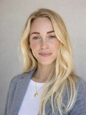 Woman with long blonde hair wearing a gray blazer and a gold necklace.
