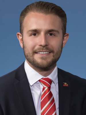 Man in suit with red striped tie smiling against blue background.