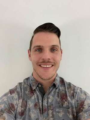 Luke Cunningham wearing a camouflage collared shirt smiling against a white background