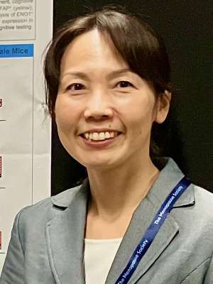 Smiling woman in a gray blazer wearing a lanyard beside a research poster