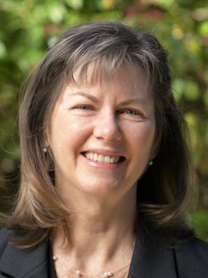 Head-and-shoulders portrait of person in blazer and leafy background
