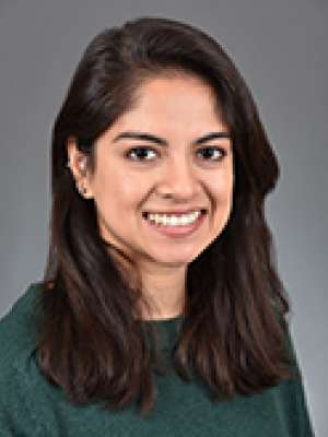 Smiling woman with dark hair in green sweater against gray background