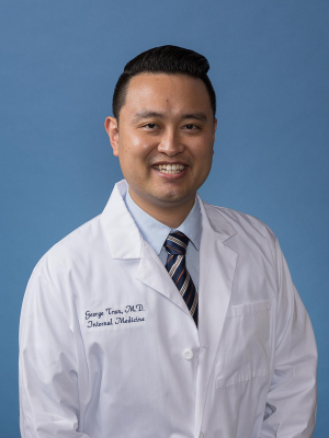 Smiling doctor in white coat and striped tie against blue background.