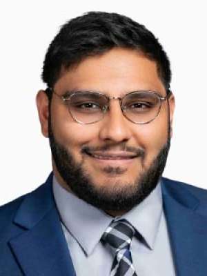 Man in navy suit and striped tie wearing glasses, smiling in professional headshot.