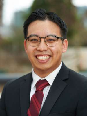 Smiling professional headshot of person in suit, glasses and red striped tie.